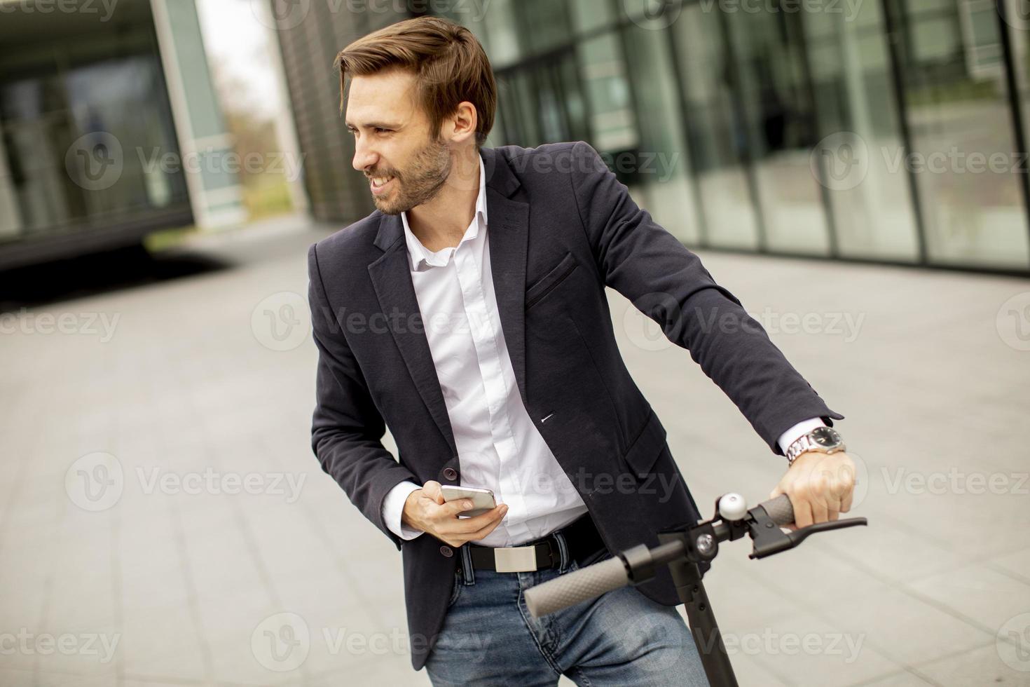 Joven empresario mediante teléfono móvil en scooter eléctrico foto