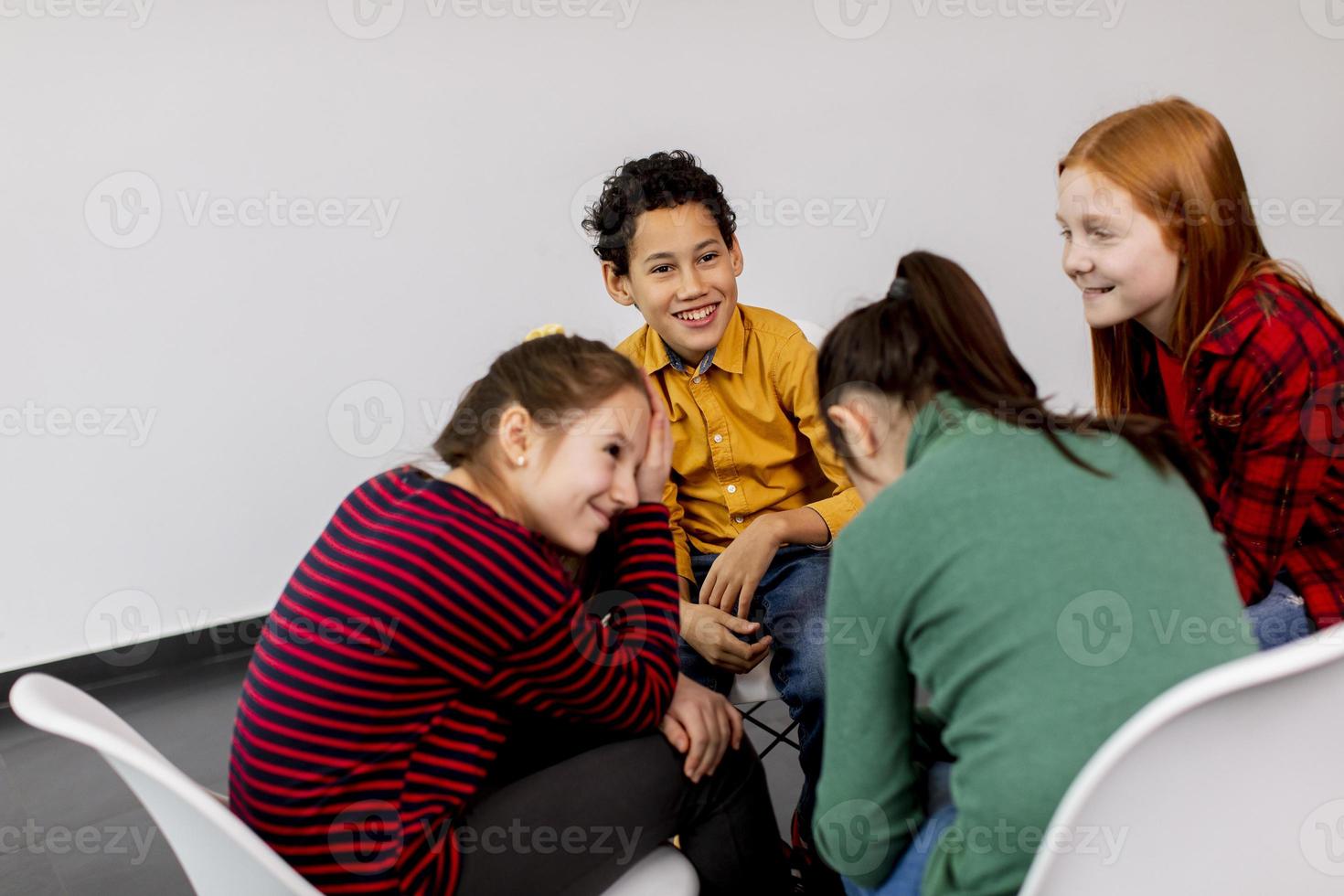 Portrait of cute little kids in jeans  talking and sitting in chairs against white wall photo