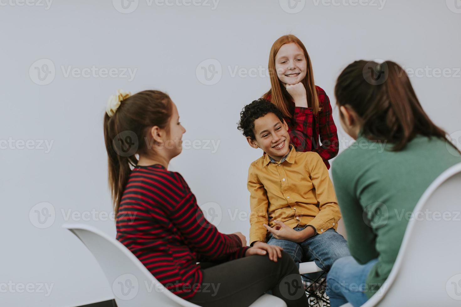 Portrait of cute little kids in jeans  talking and sitting in chairs against white wall photo