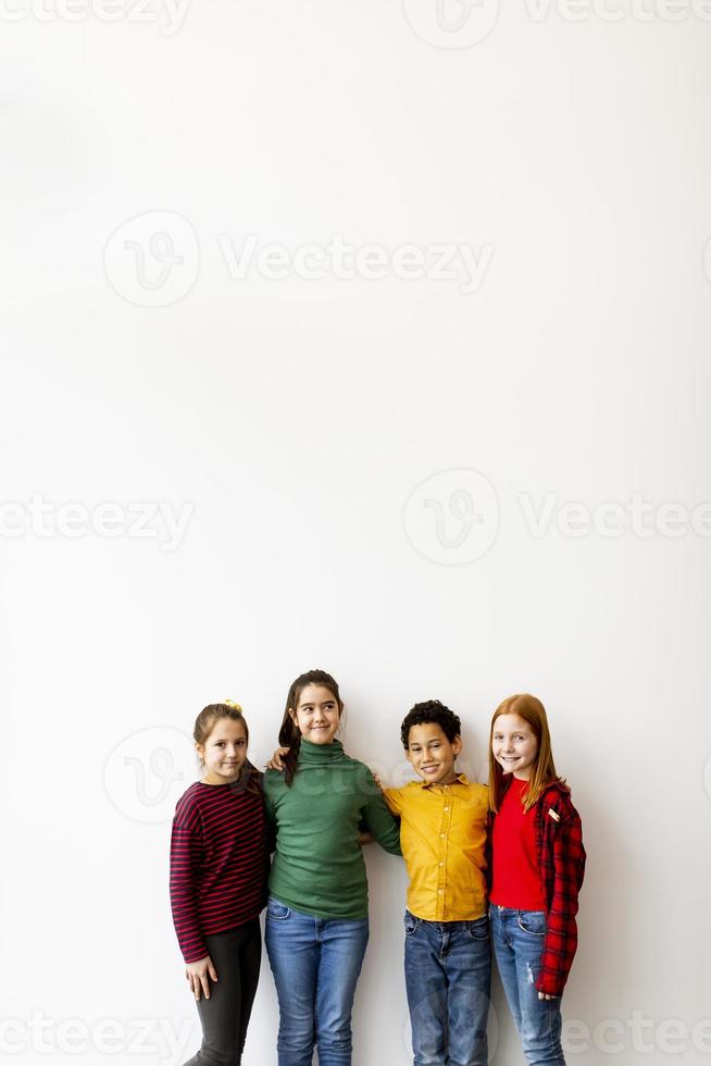 Retrato de lindos niños pequeños en jeans mirando a la cámara y sonriendo mientras está de pie contra la pared blanca foto