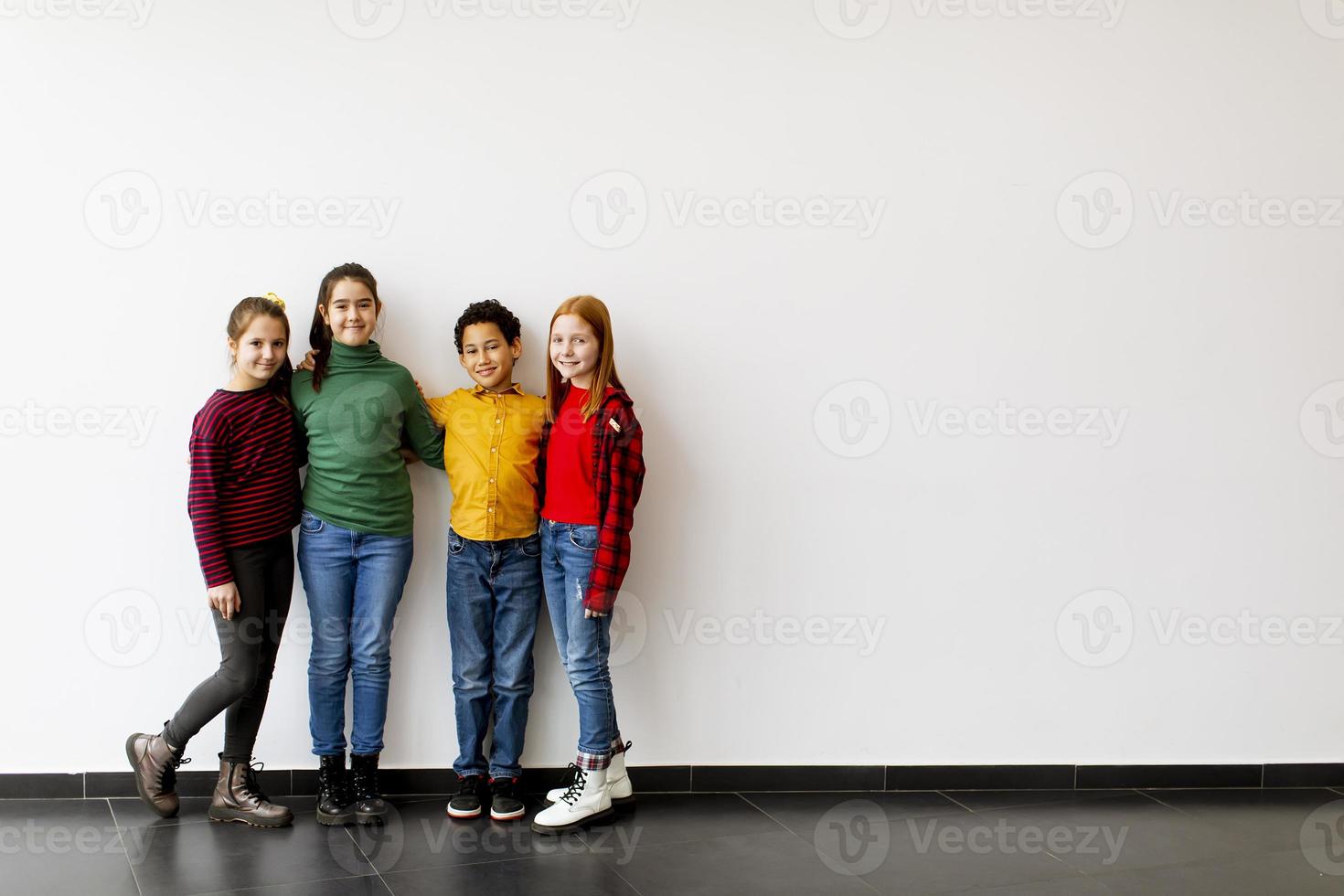 Retrato de niños pequeños lindos en jeans mirando a la cámara y sonriendo de pie contra la pared blanca foto