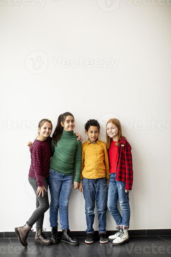 Portrait of cute little kids in jeans looking at camera and smiling standing against white wall photo