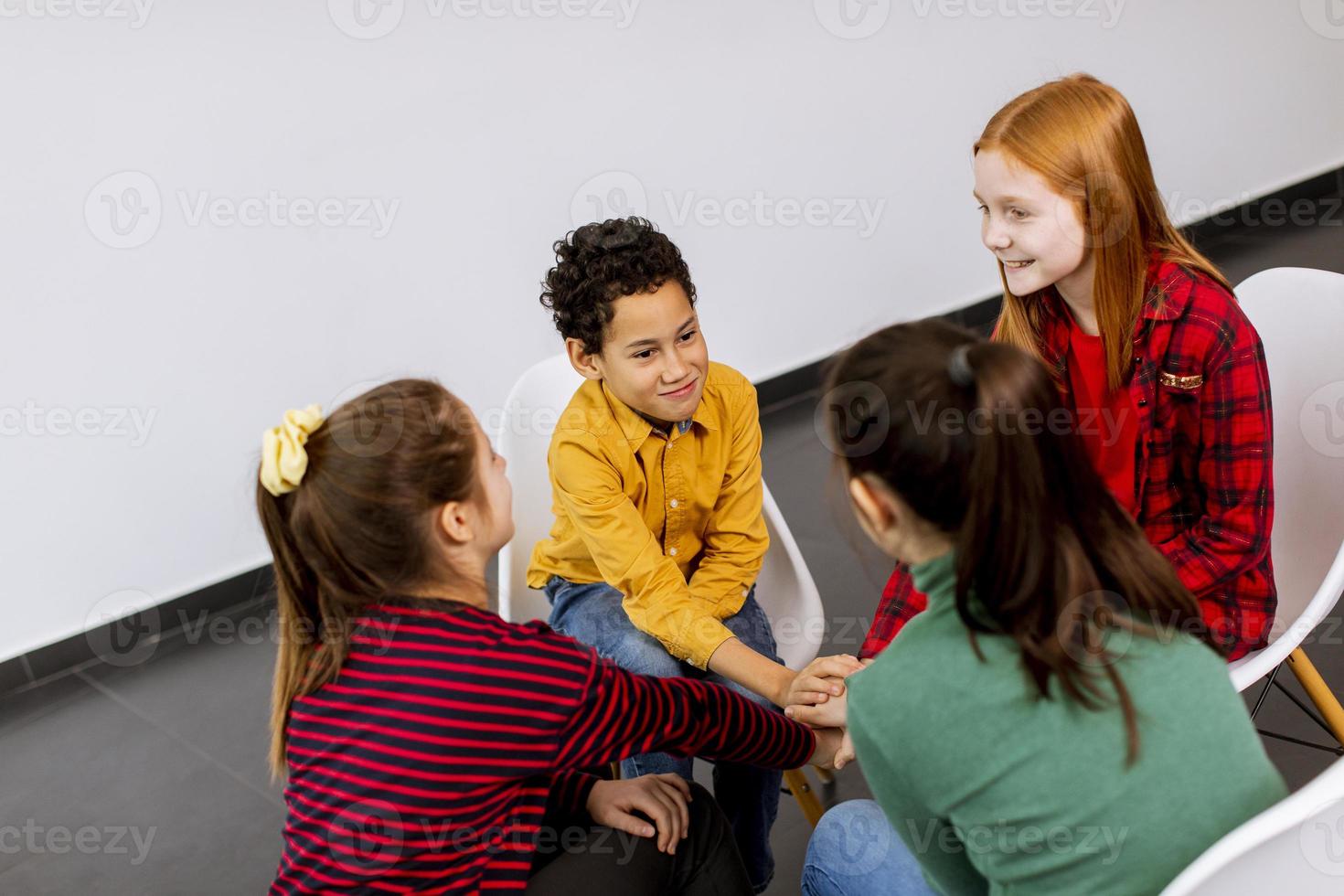 Retrato de lindos niños pequeños en jeans hablando y sentados en sillas contra la pared blanca foto