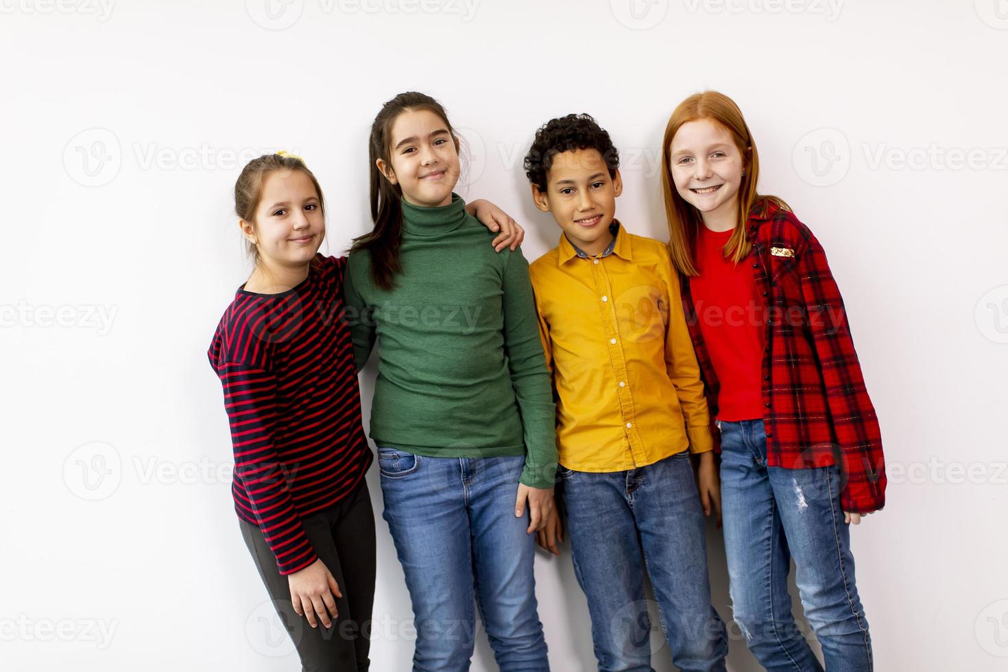 Retrato de niños pequeños lindos en jeans mirando a la cámara y sonriendo de pie contra la pared blanca foto