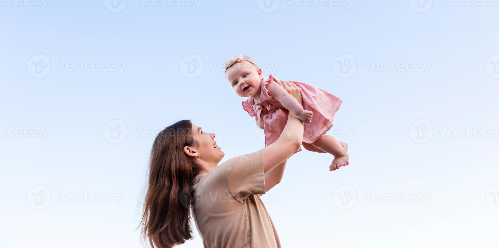 Young mother holds baby daughter in the air and laughing in the sky photo