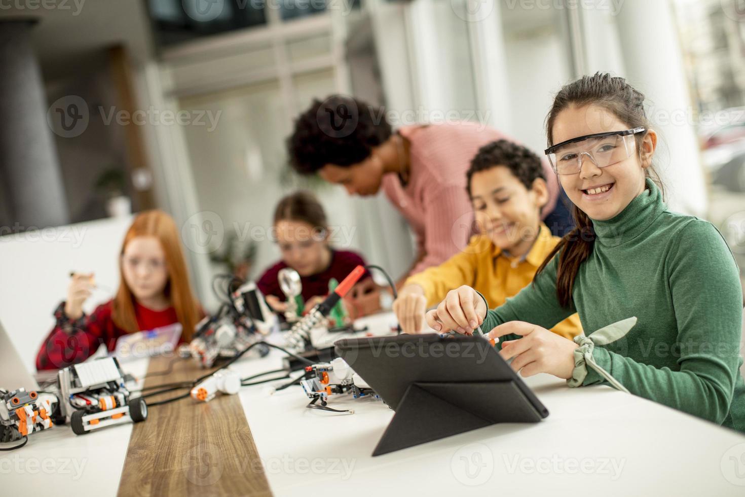 Niños felices con su profesora de ciencias afroamericana con programación de portátiles, juguetes eléctricos y robots en el aula de robótica foto
