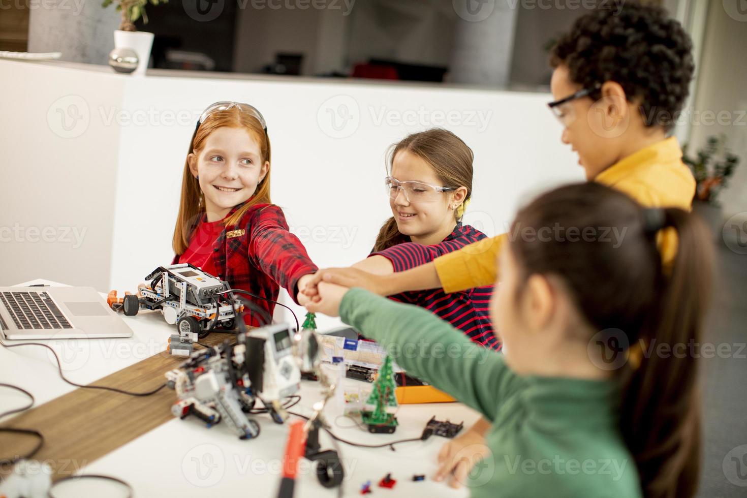 Niños felices programando juguetes eléctricos y robots en el aula de robótica foto