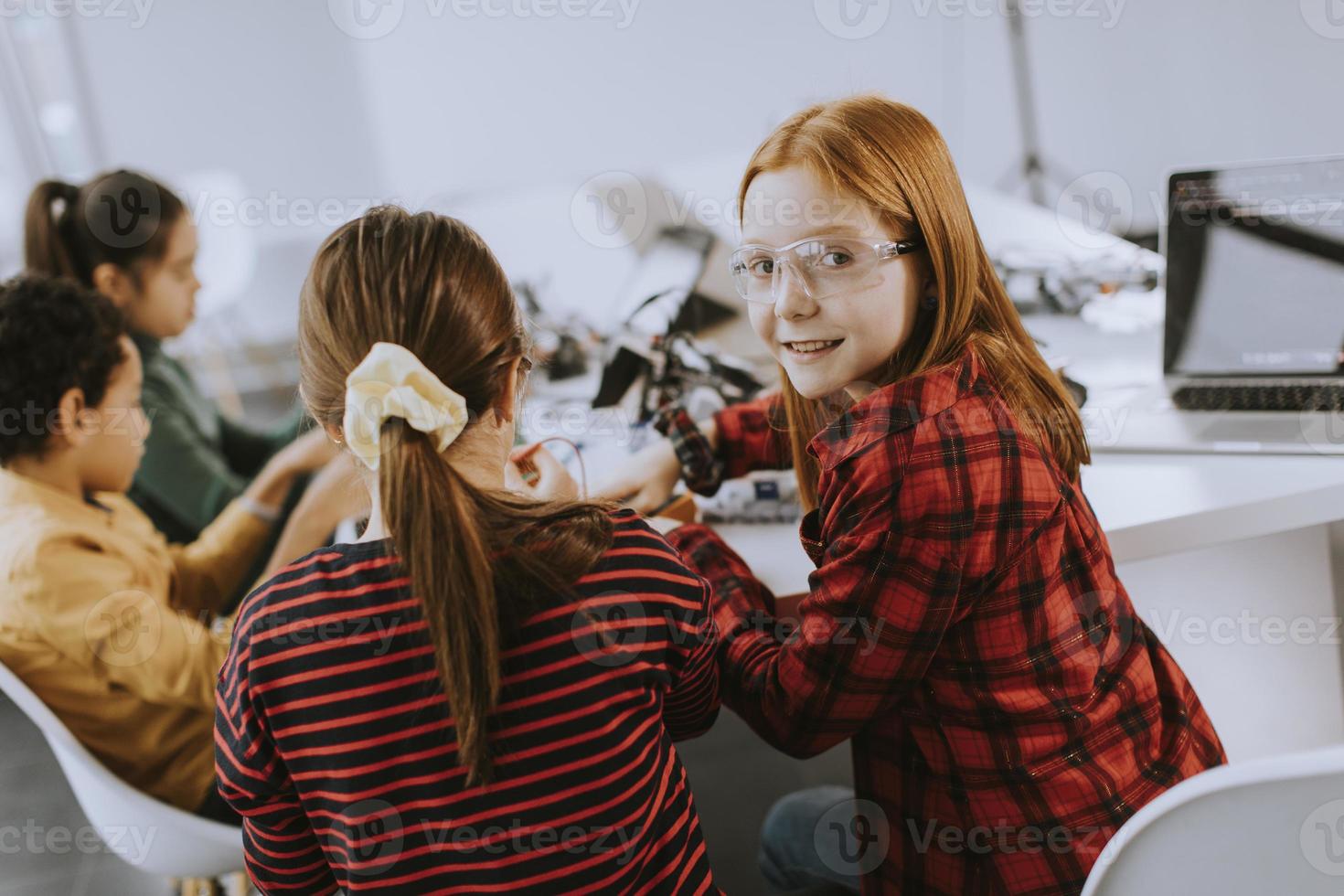 Niños felices programando juguetes eléctricos y robots en el aula de robótica foto