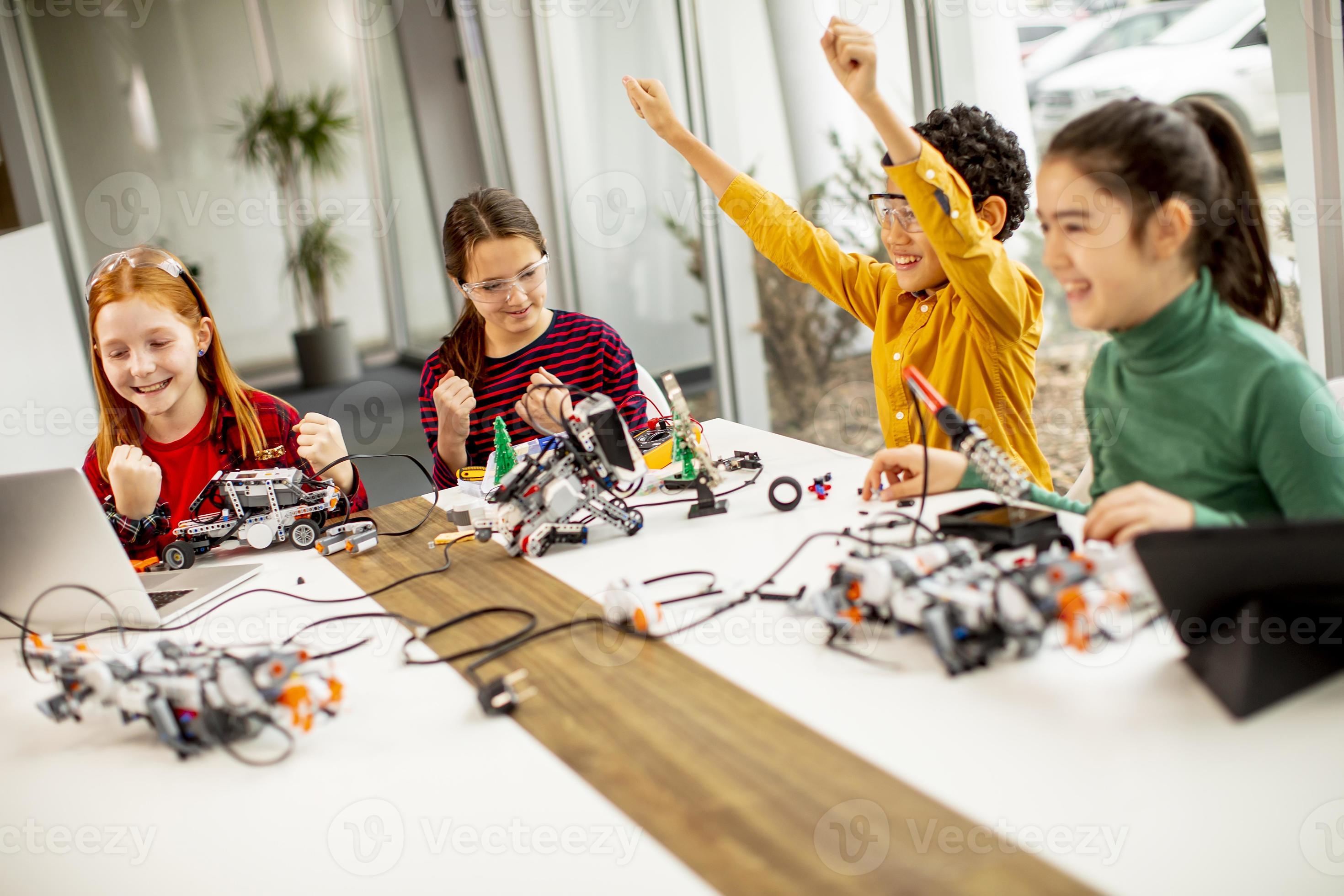 Happy kids programming electric toys and robots at robotics classroom ...