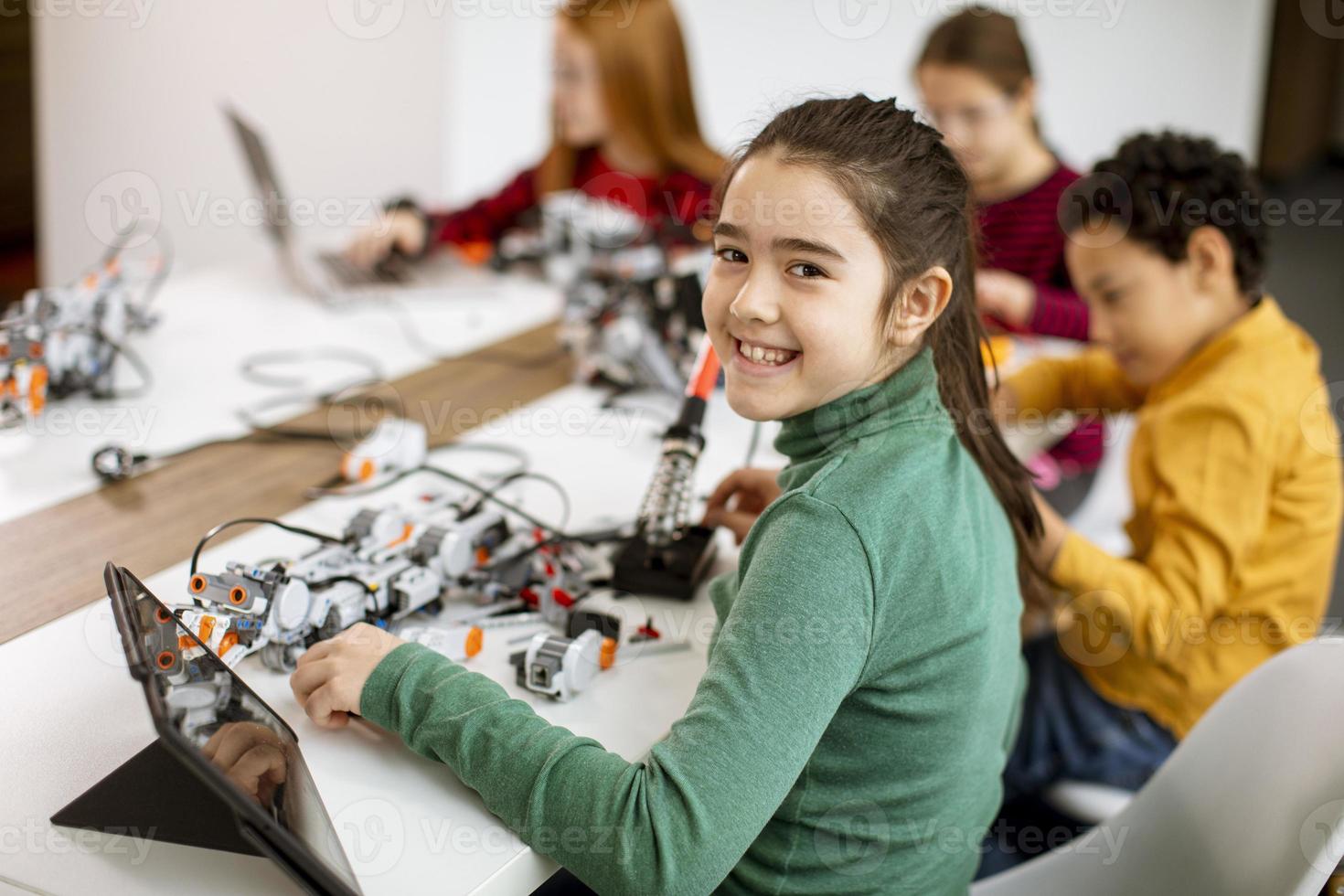 Niños felices programando juguetes eléctricos y robots en el aula de robótica foto