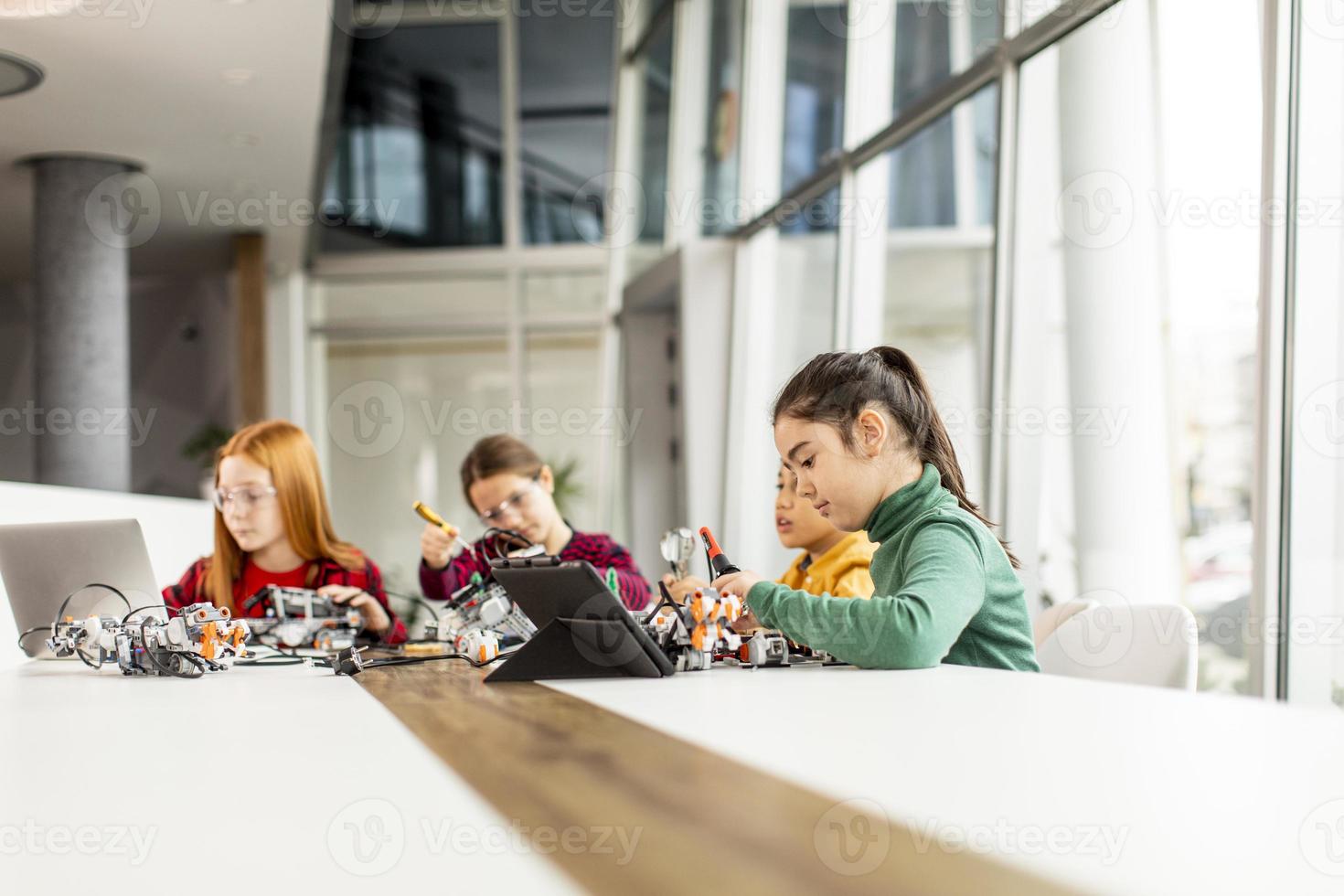 Niños felices programando juguetes eléctricos y robots en el aula de robótica foto