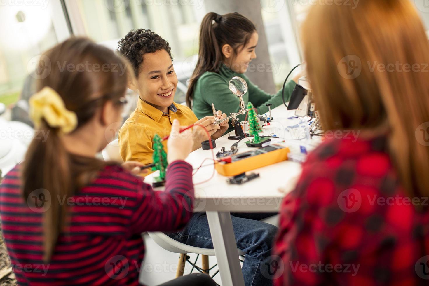 Niños felices programando juguetes eléctricos y robots en el aula de robótica foto