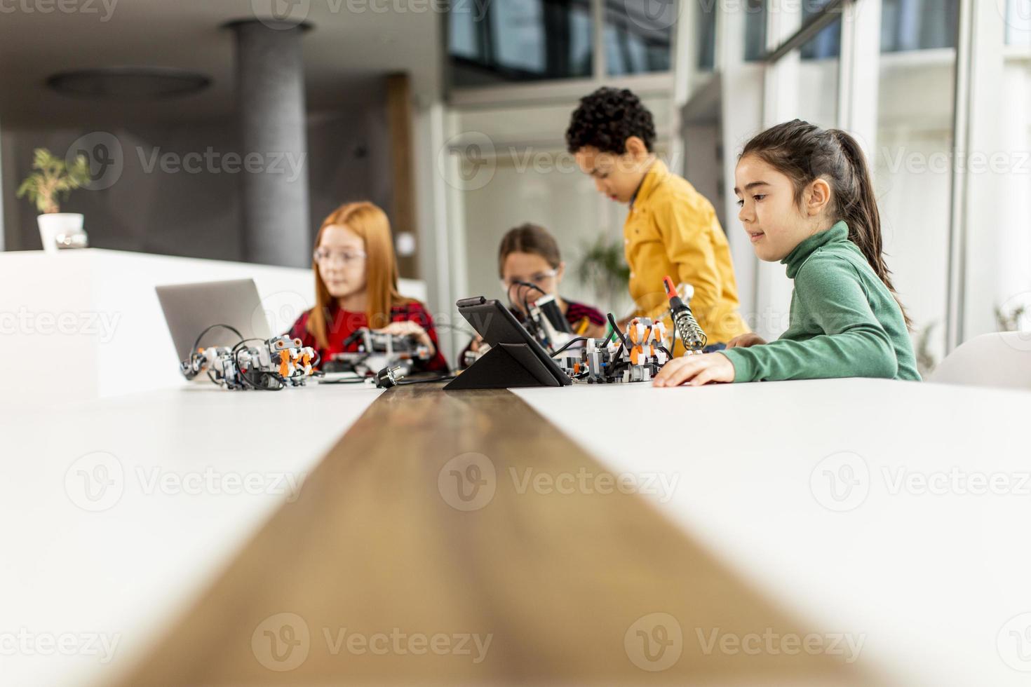 Niños felices programando juguetes eléctricos y robots en el aula de robótica foto