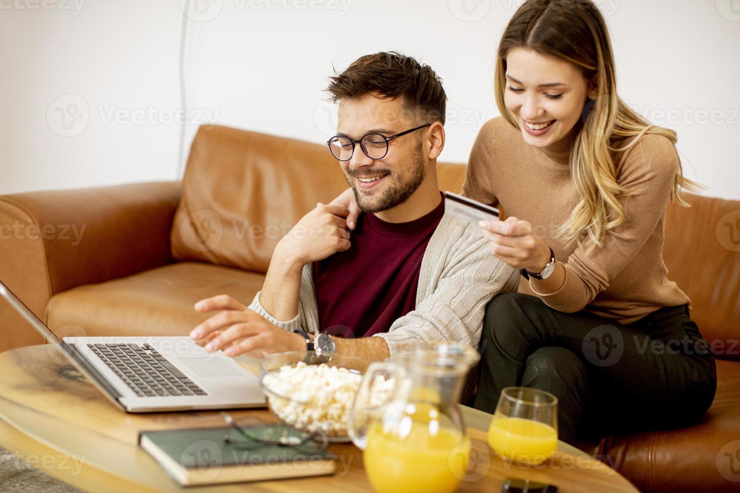 Young woman and young man using laptop for onlin payment while sitting by sofa at home photo