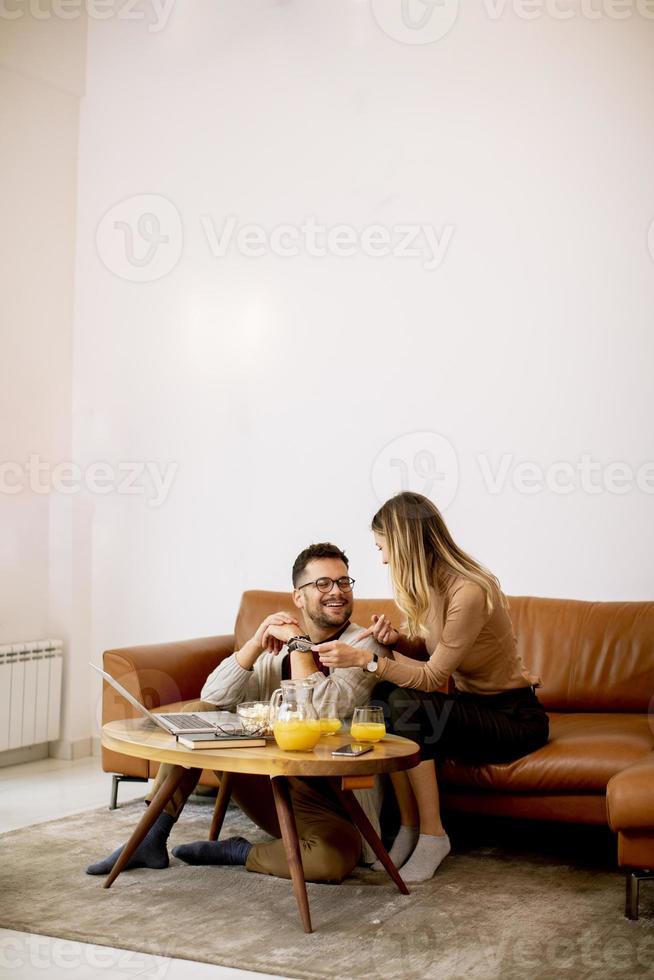 Young woman and young man using laptop for onlin payment while sitting by sofa at home photo