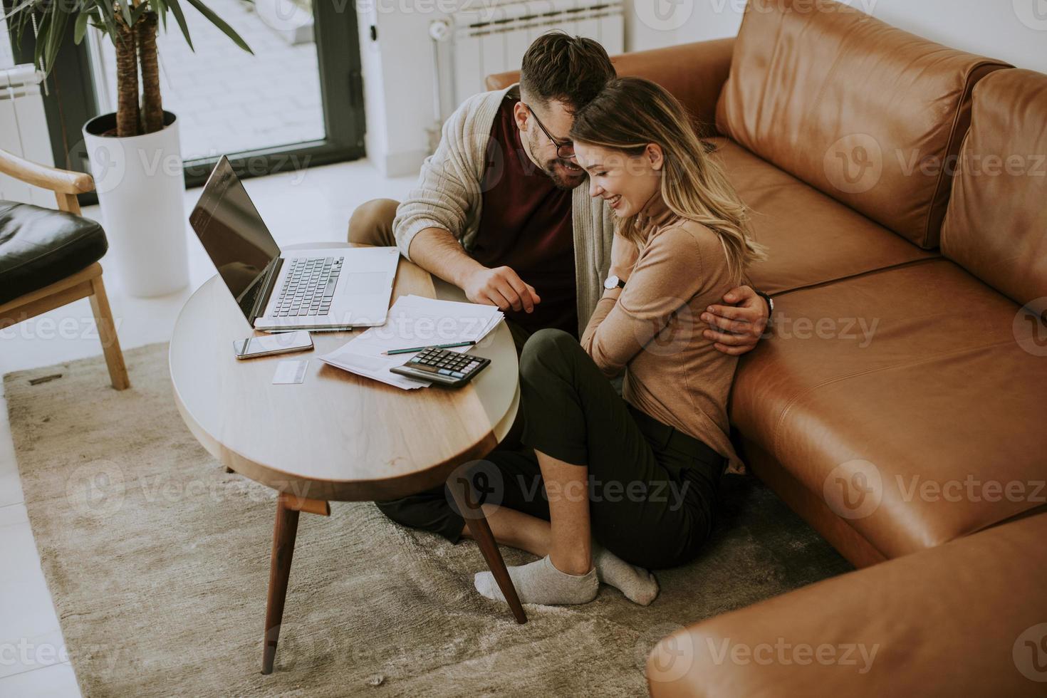 Young woman and young man using laptop while sitting by sofa at home photo