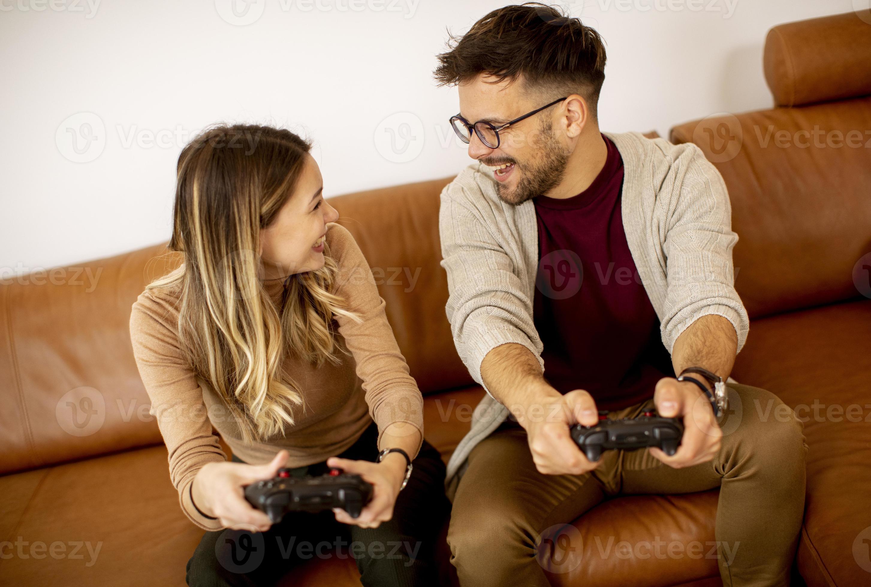 Happy Couple Sitting on the Sofa Playing Video Games, Using Controllers.  Competitive Girlfriend and Boyfriend in Love have Fun Playing in Online  Video Games at Home Together. Close-up Focus on Hands Stock