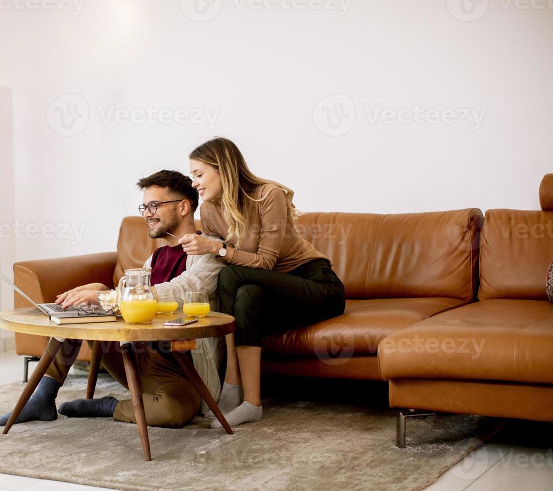 Young woman and young man using laptop for onlin payment while sitting by sofa at home photo