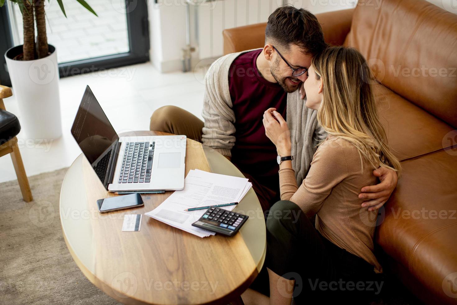 Young woman and young man using laptop while sitting by sofa at home photo