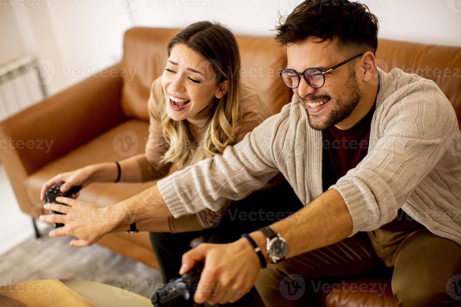 Young couple playing video games at home sitting on sofa and enjoying themselves photo