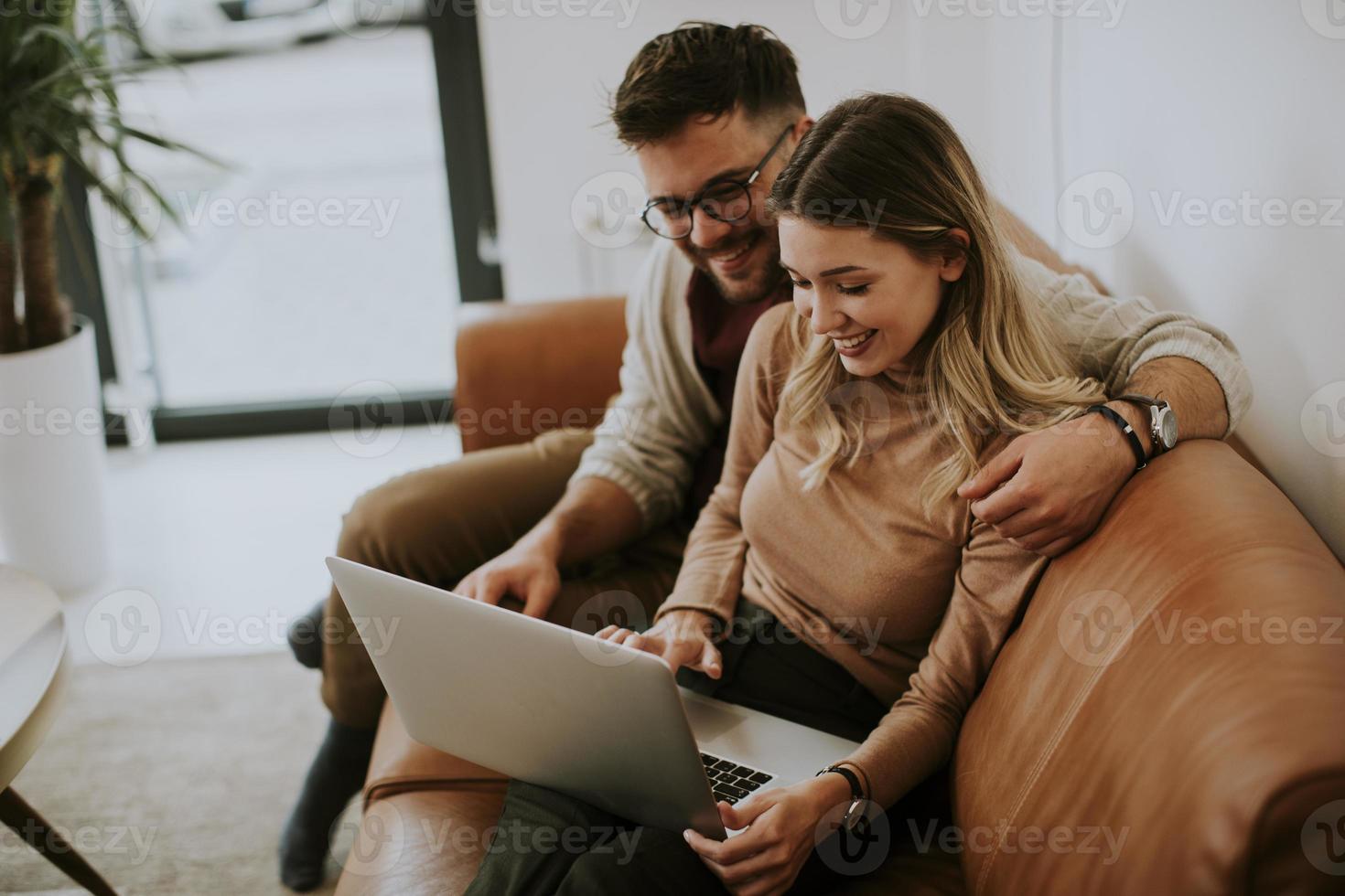 Pareja joven usando la computadora portátil juntos mientras está sentado en el sofá en casa foto