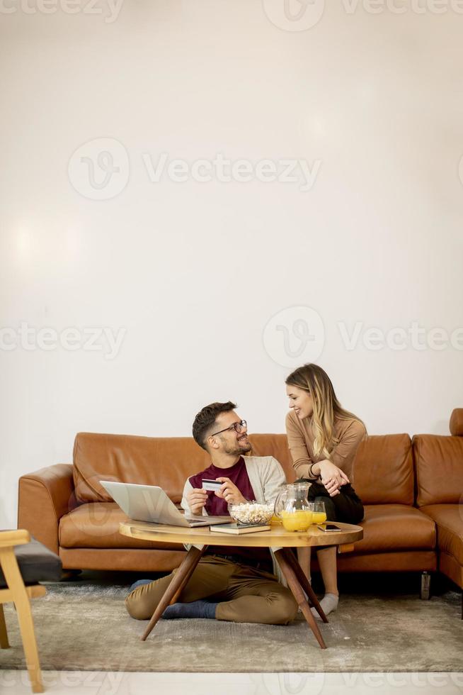Mujer joven y hombre joven con ordenador portátil para pago onlin mientras está sentado en el sofá en casa foto
