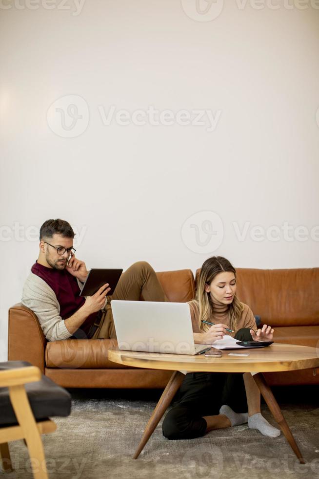 Young woman and young man using laptop while sitting by sofa at home photo