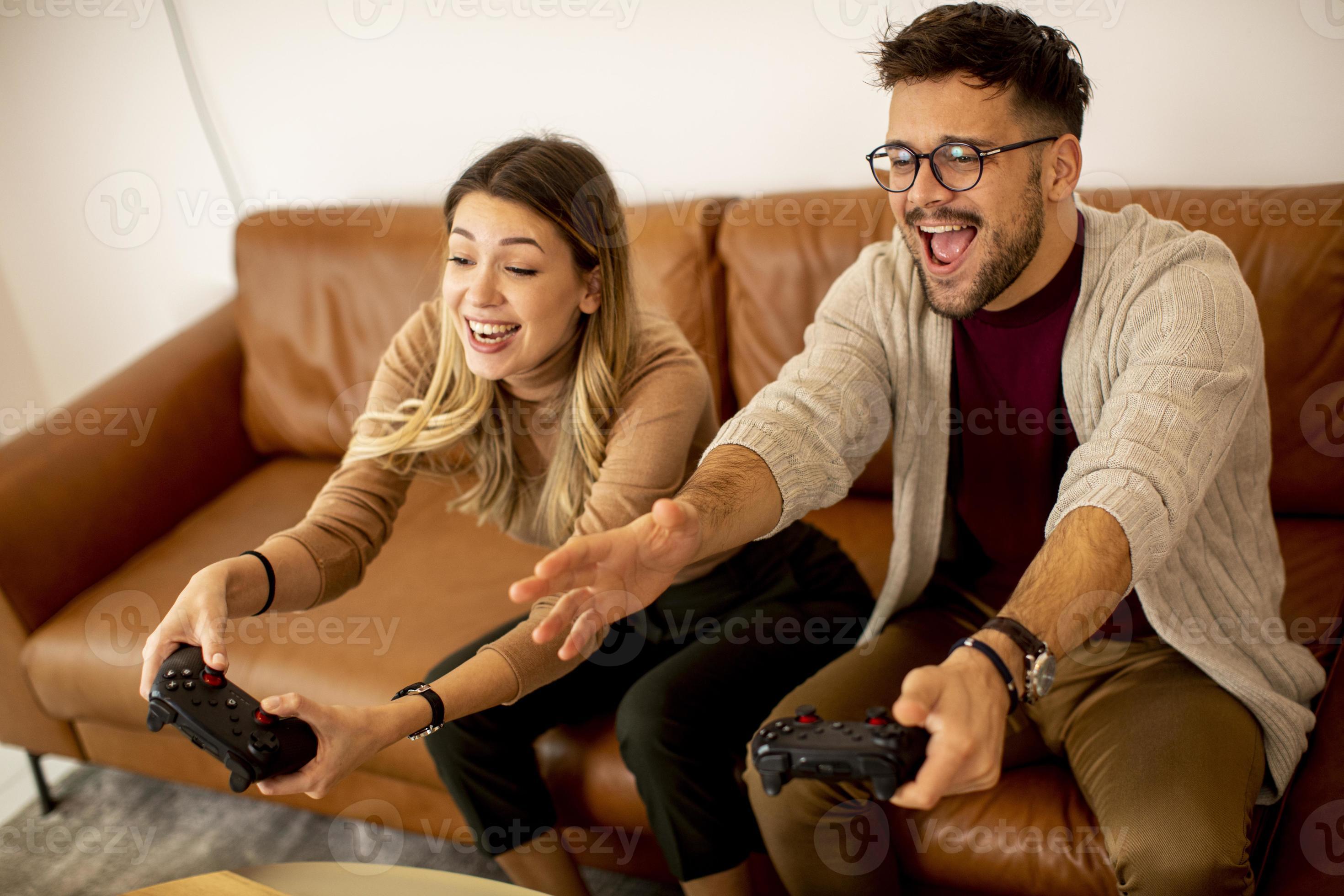 Happy Couple Sitting on the Sofa Playing Video Games, Using Controllers.  Competitive Girlfriend and Boyfriend in Love have Fun Playing in Online  Video Games at Home Together. Close-up Focus on Hands Stock