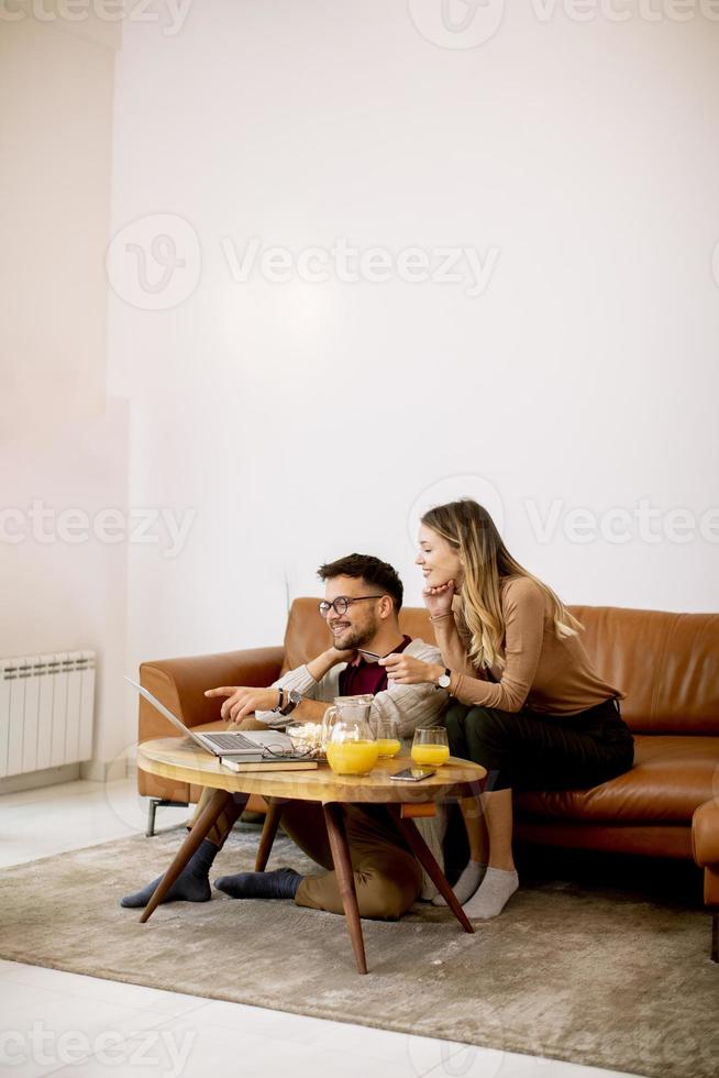 Young woman and young man using laptop for onlin payment while sitting by sofa at home photo