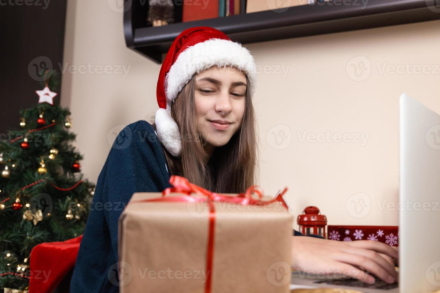 niña con sombrero de santa claus usando laptop para videollamadas a amigos y padres foto