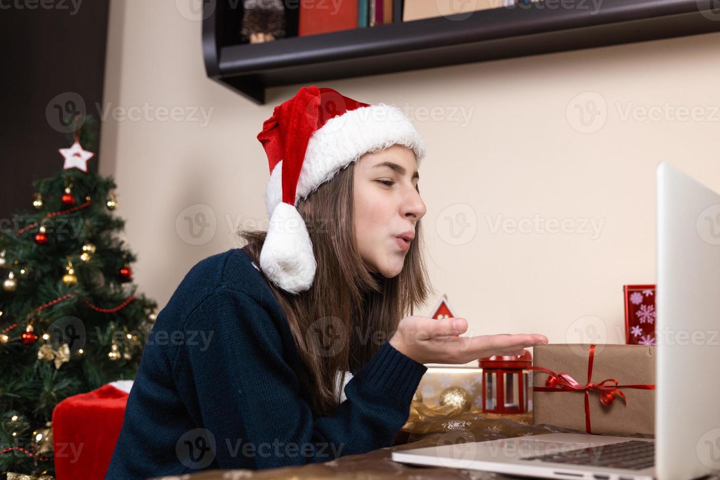 Girl in santa claus hat using laptop for video call to friends and parents photo