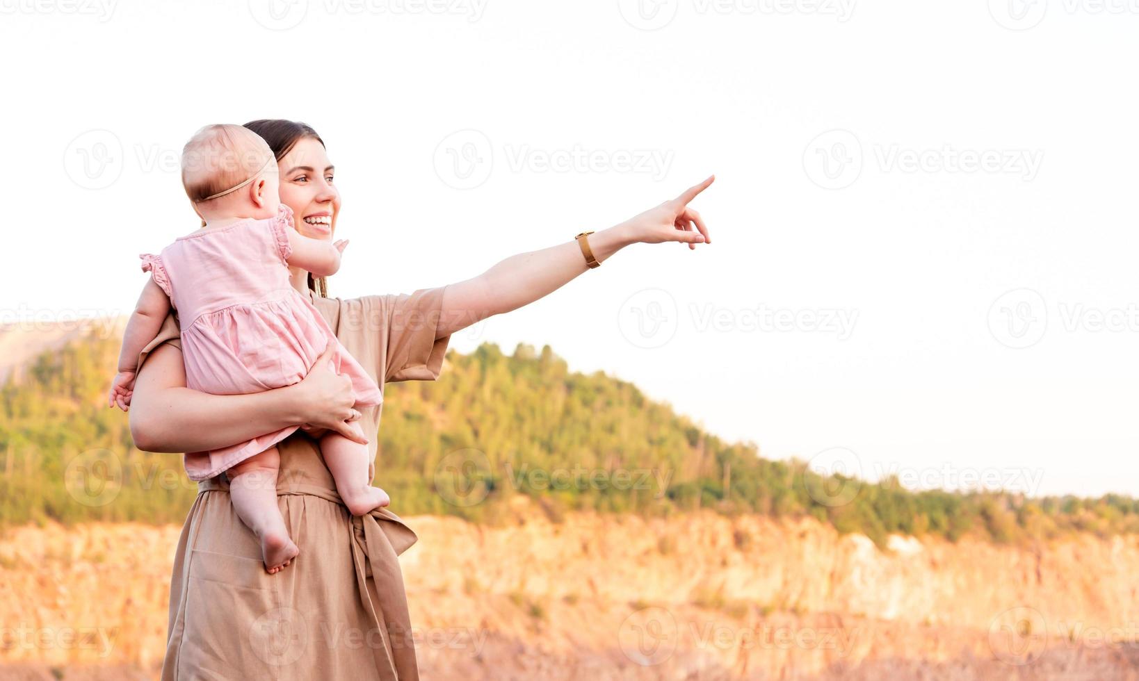 feliz madre sostiene a su hija mirando a otro lado y apuntando foto