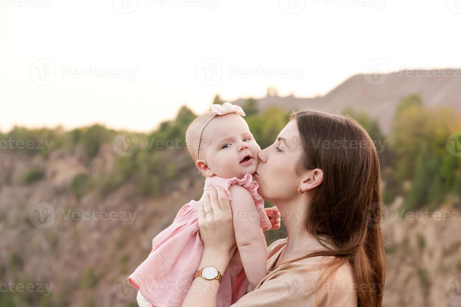 mamá sostiene a un niño en sus brazos y lo besa suavemente en la mejilla al aire libre foto