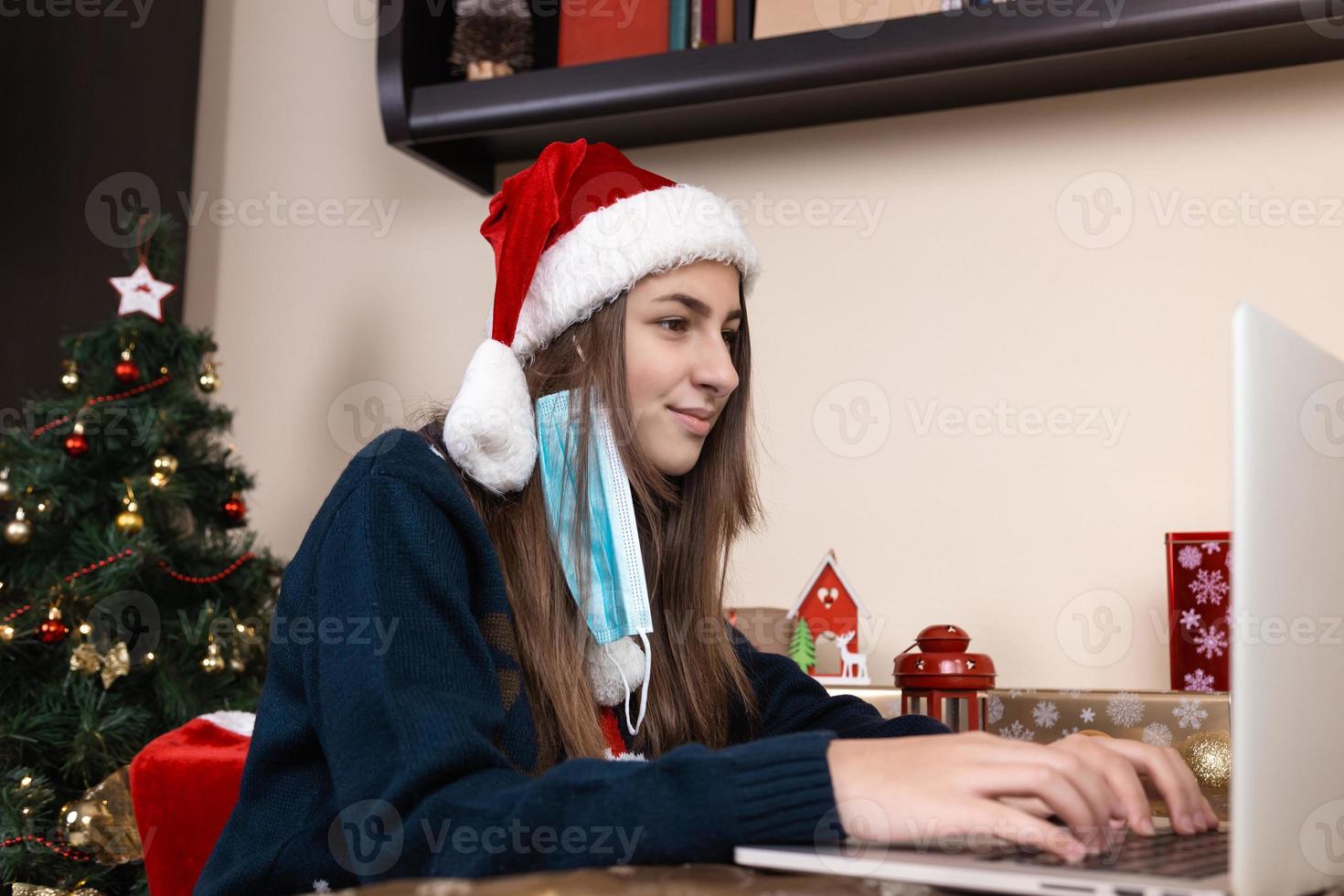 Girl in santa claus hat using laptop for video call to friends and parents photo