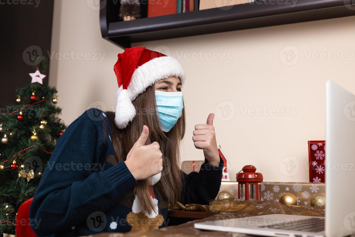 Girl in santa claus hat using laptop for video call to friends and parents photo