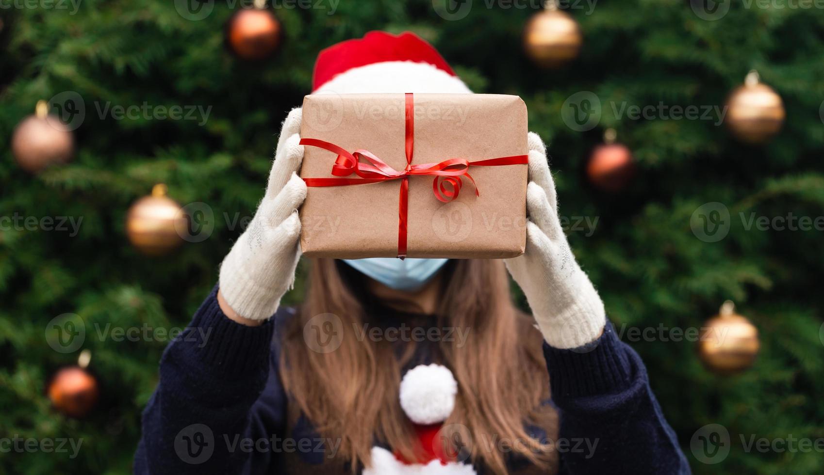 Faceless portrait of a woman holding gift box with red ribbon on a Christmas background photo