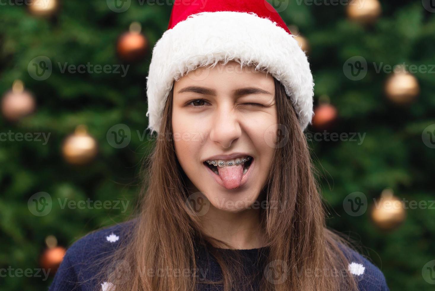 Close-up portrait of woman wearing a santa claus hat with emotion sticking tongue out photo