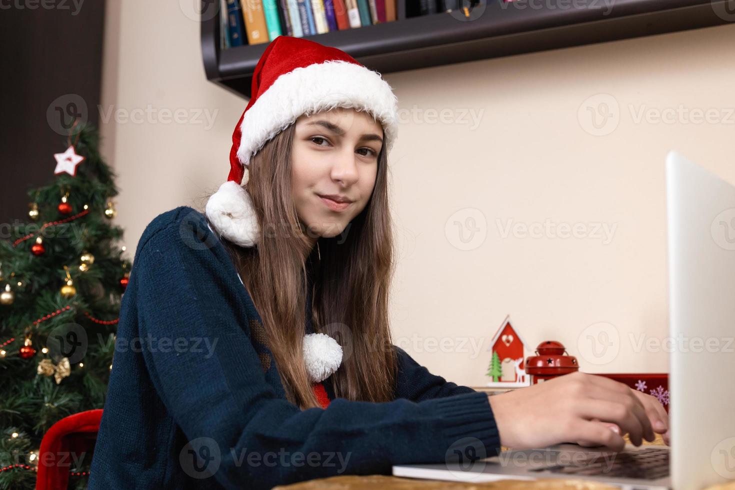 Girl in santa claus hat talks using laptop photo