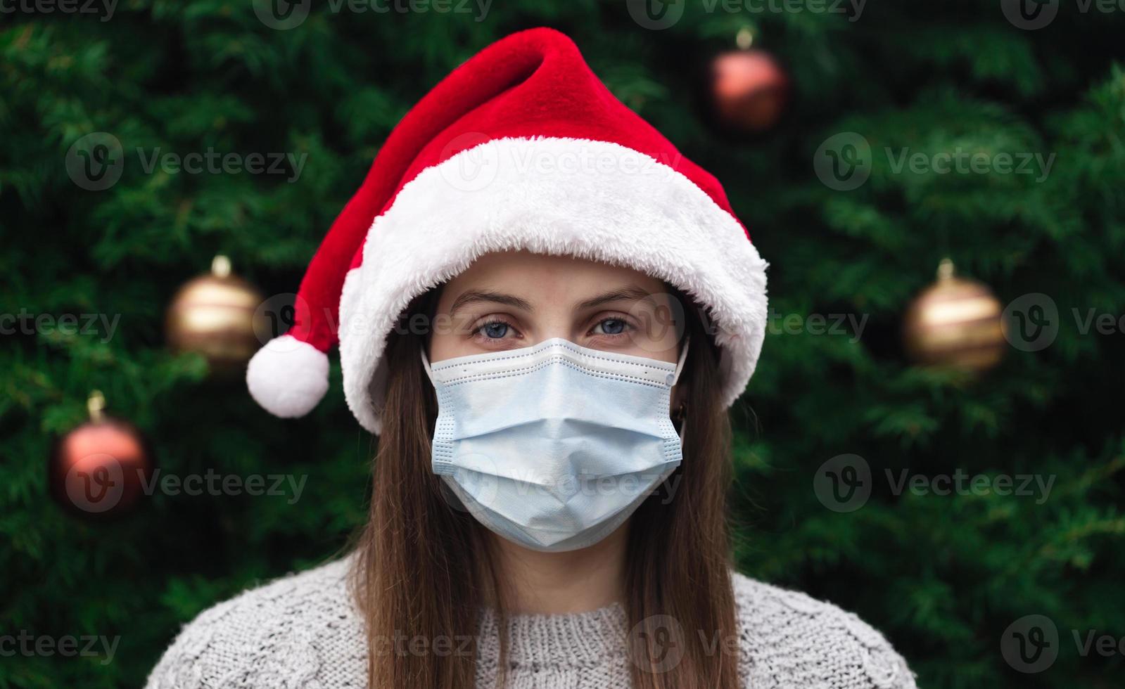 Close-up portrait of woman wearing a santa claus hat and medical mask with emotion photo