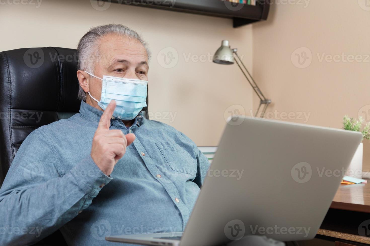 Senior man in face mask working or communicating on laptop at home photo