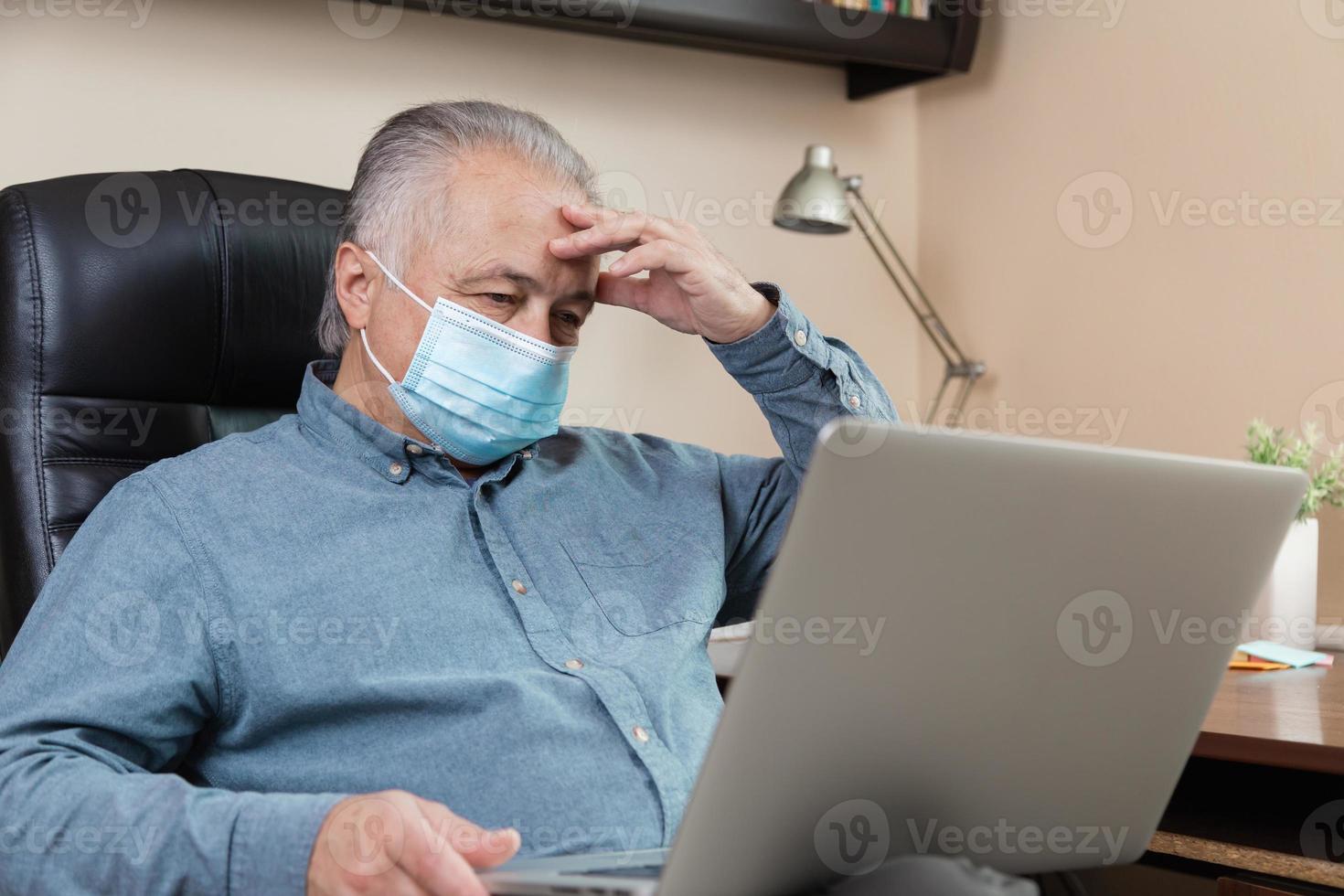 Senior man in face mask working or communicating on laptop at home photo