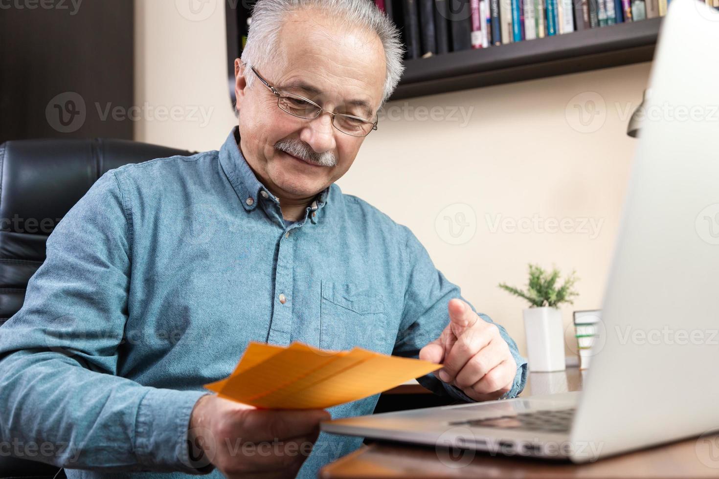 Hombre senior en mascarilla trabajando o comunicándose en un portátil en casa foto