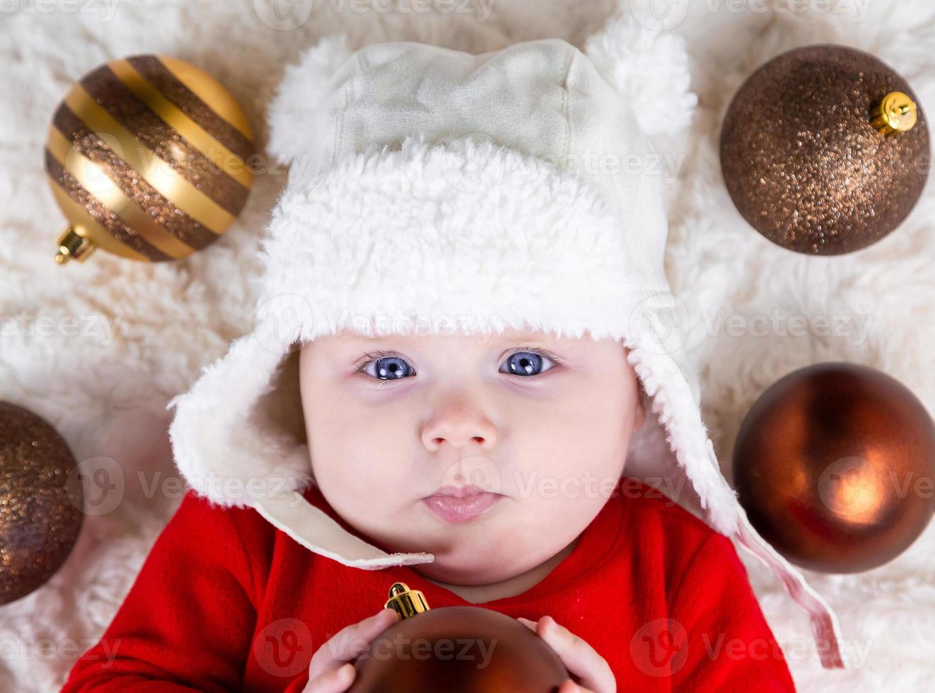 lindo bebé mordiendo la bola de navidad tirado en el suelo foto