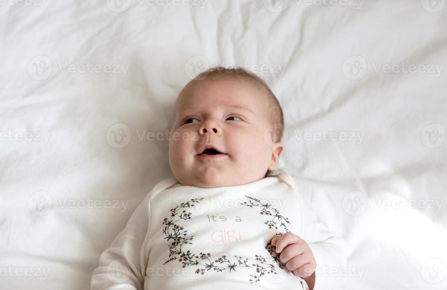 A close-up portrait of a baby girl who lies in bed and smiles photo