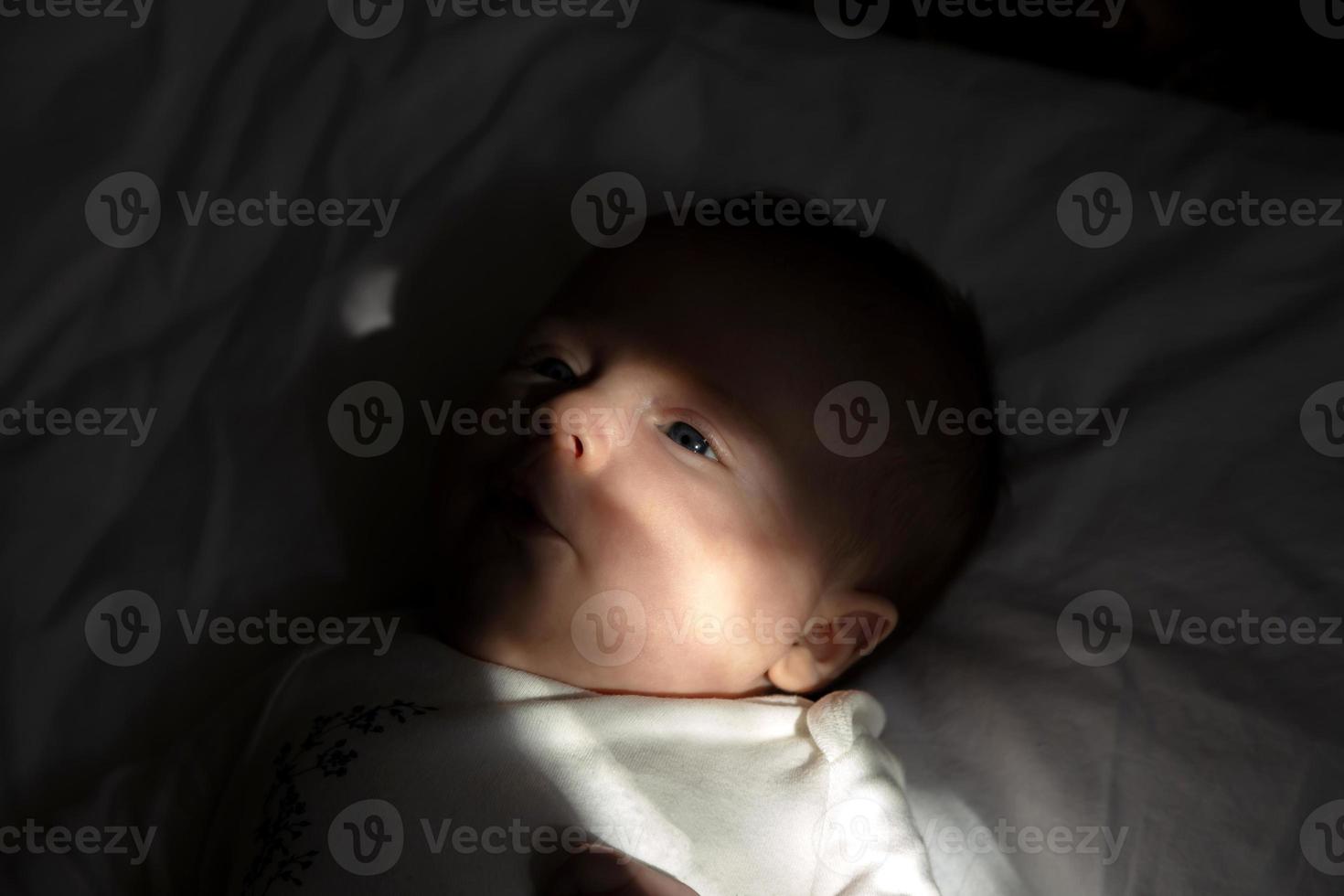 A closeup portrait of a baby girl lying on a bed in the sun 2429674