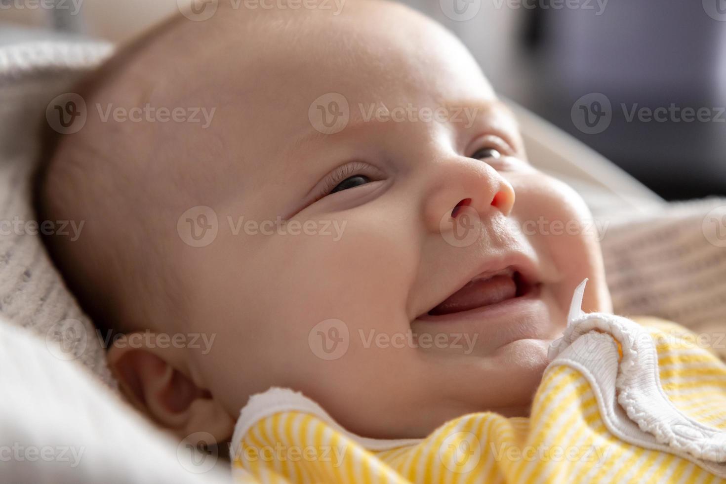 A close-up portrait of a baby girl who lies in bed and smiles photo