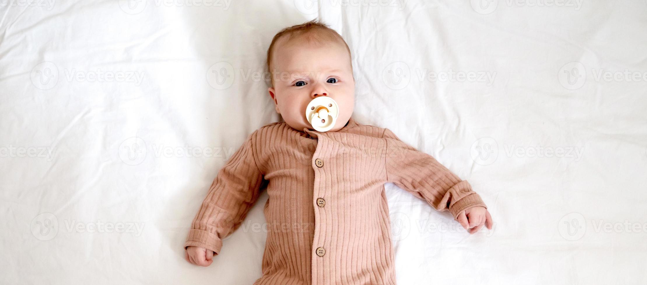 Portrait of a newborn baby girl who lies on a bed with a nipple soother photo