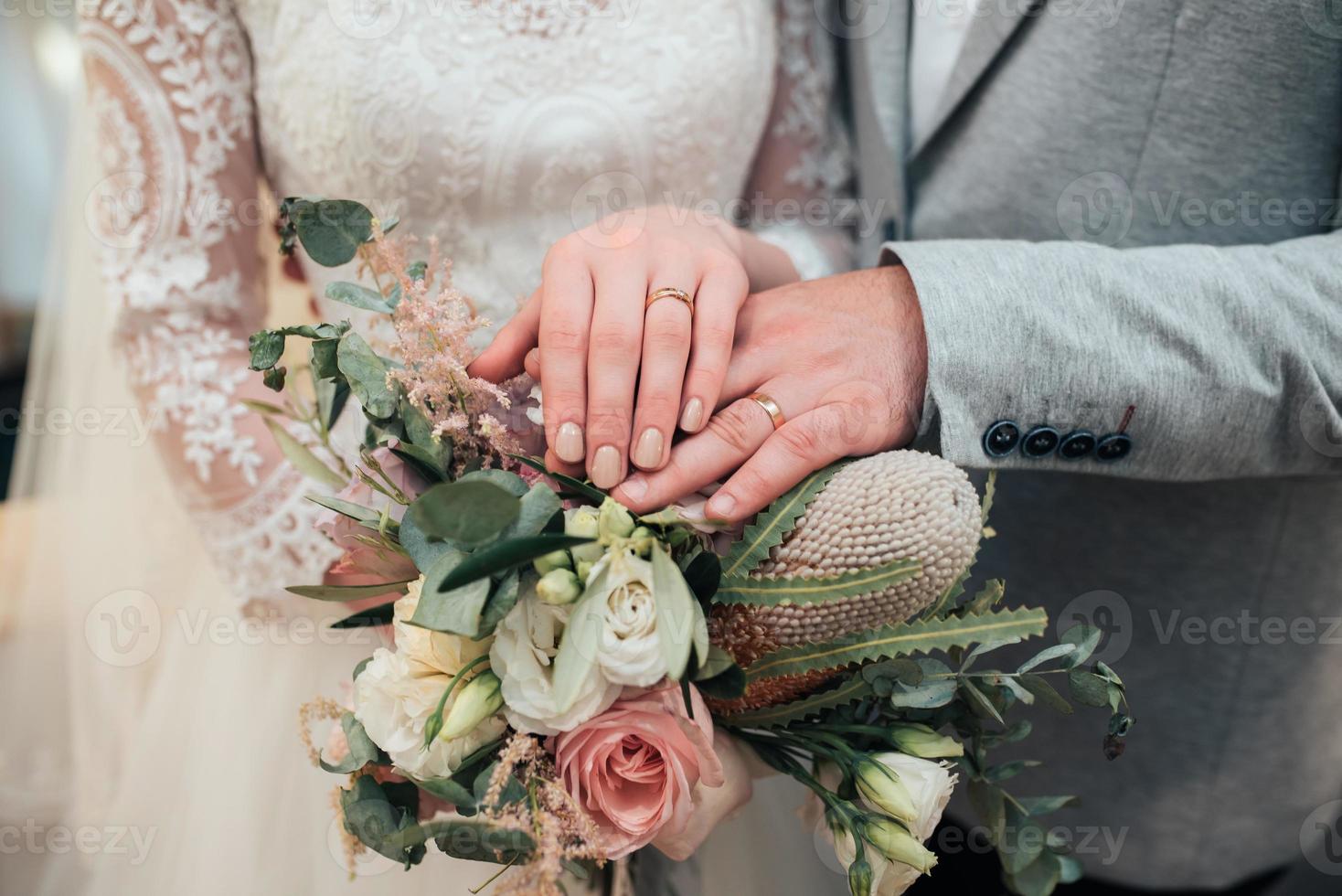 Manos con anillos de la novia y el novio están acostados en el primer ramo de flores foto