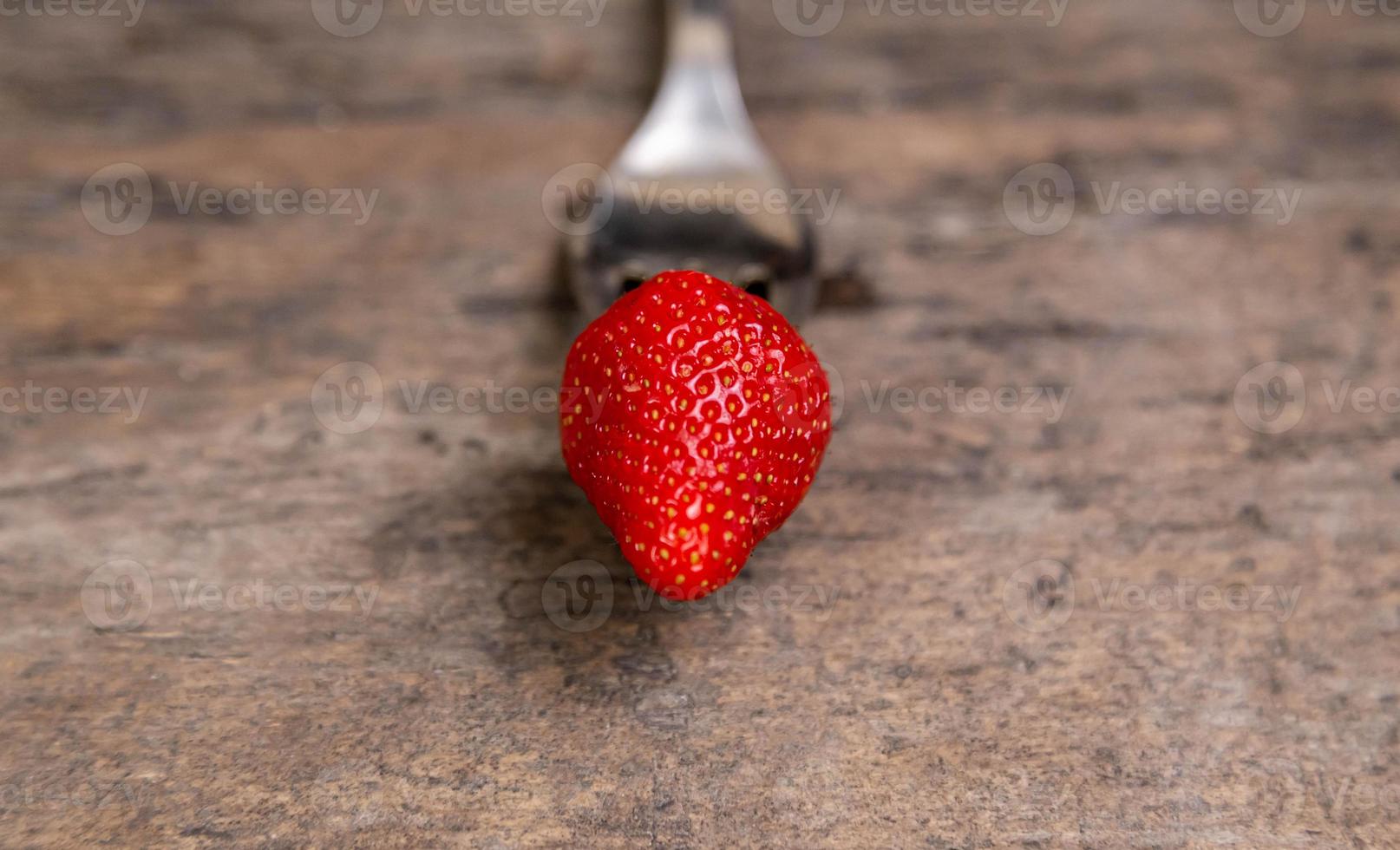 One strawberry on golden fork on wooden non paint background photo