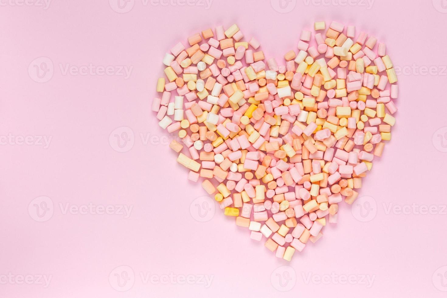 Top view of the multicolored marshmallows which lies in the shape of a heart on a monochrome pink background photo